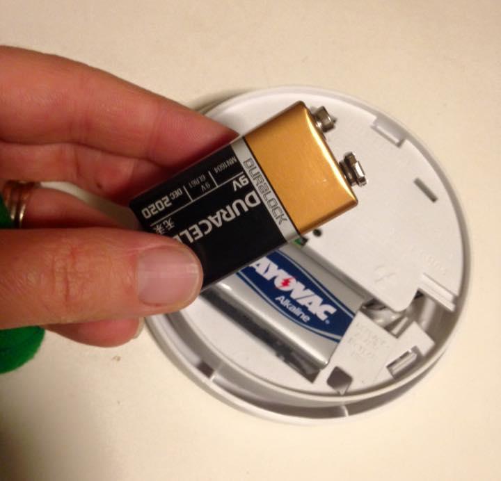 Someone putting a battery in a smoke alarm.