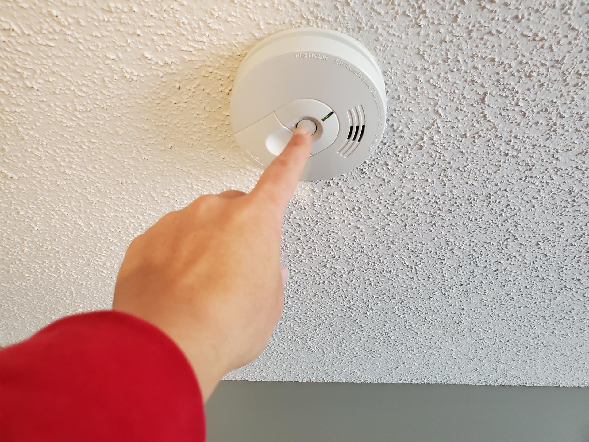 Someone pressing a smoke alarm test button.