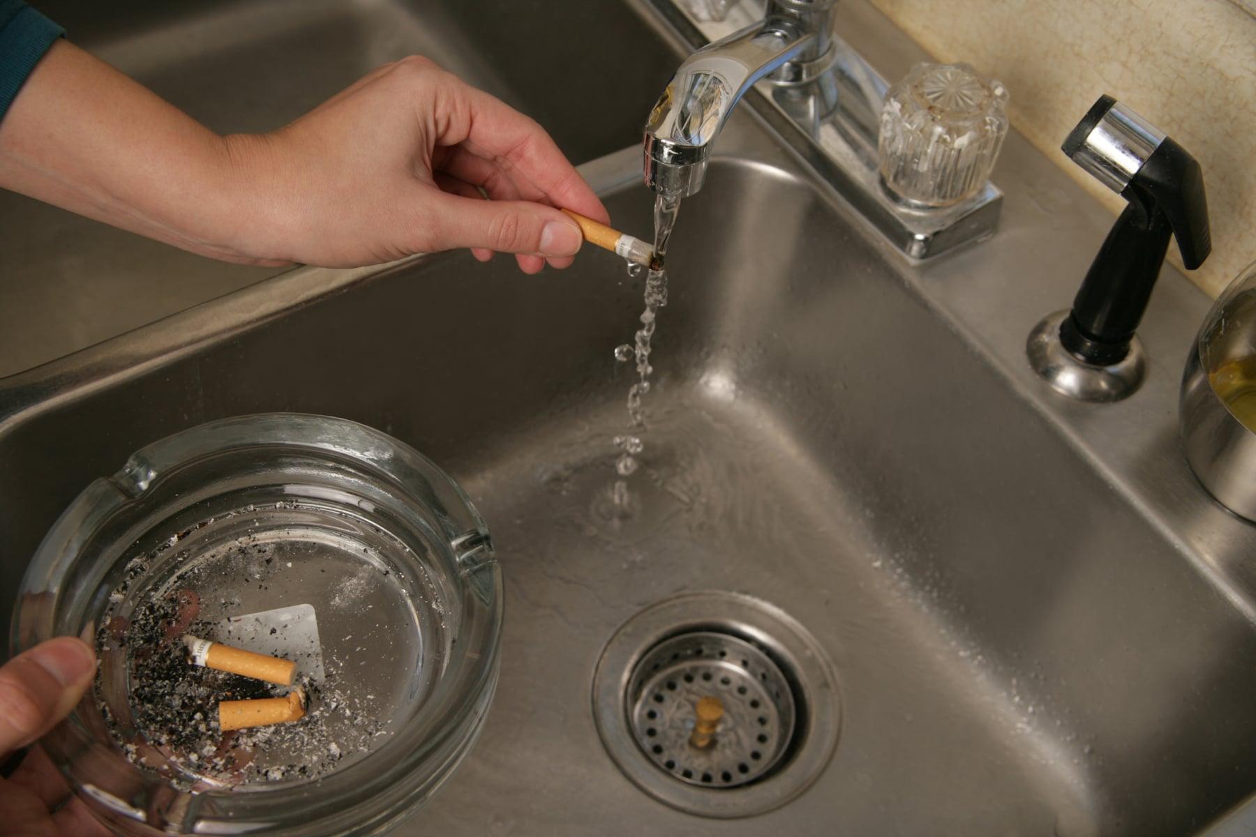 A woman runs a cigarette under water to put it out.